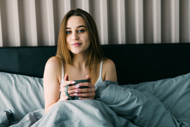休息一个年轻女子在家里的床上喝咖啡的画像醒来房子茶