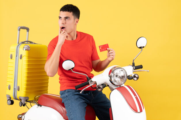 轻便摩托车正面图：一个穿着红色t恤的年轻人骑着轻便摩托车 手里拿着信用卡年轻人视野红色