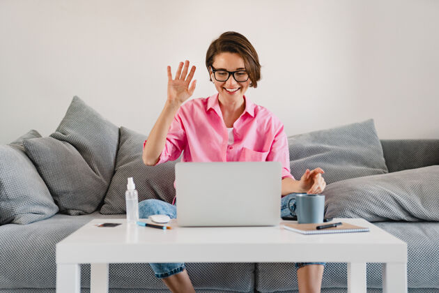 商务女性一个穿着粉色衬衫的微笑女人 在家里的沙发上轻松地坐在桌子旁 在家里用笔记本电脑上网在家工作在线办公室