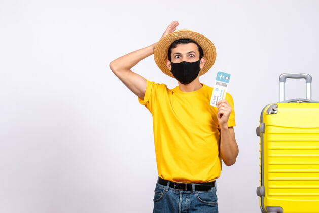 开放正面图：戴草帽的年轻人站在黄色手提箱旁 手里拿着机票视图站手提箱