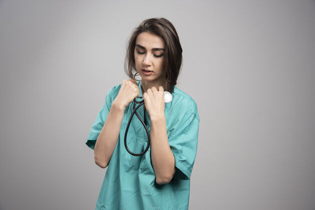 成人身着制服的年轻医生在灰色背景上使用听诊器高质量照片工作医疗健康