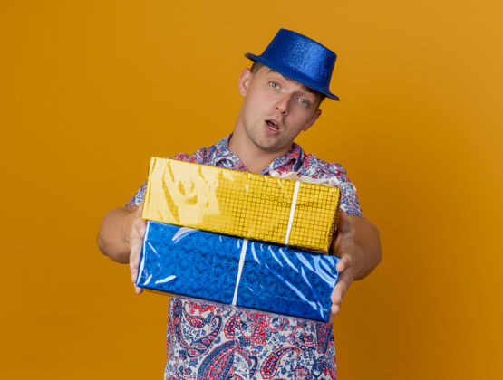 拿着戴着蓝帽子的年轻人拿着礼品盒孤立地站在橘子上礼物戴着蓝色