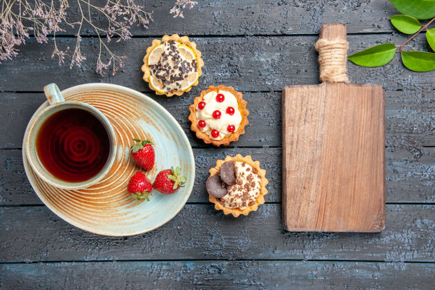 午餐顶视图一杯茶和草莓放在茶托馅饼叶上 一个砧板放在深色的木桌上健康早餐板