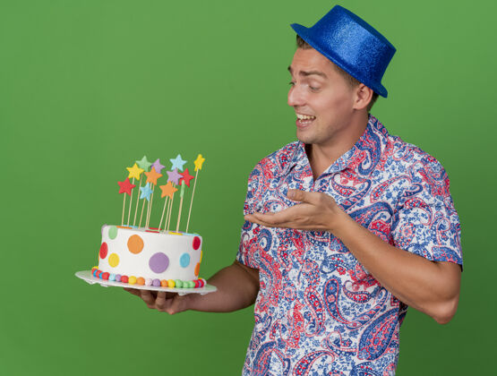点高兴的年轻人戴着蓝帽子拿着聚会 用手指着绿色的蛋糕小伙子年轻拿着