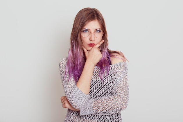 不快乐严格严肃的女性 淡紫色头发 手指放在下巴上 思考重要的事情或麻烦 穿着时髦的衬衫 在灰色的墙上摆出孤立的姿势女人随意淑女