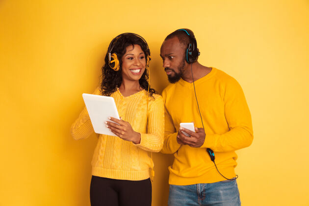 广告年轻感性的非裔美国人 穿着黄色背景的明亮休闲服美丽的情侣人类情感的概念 面部表情 关系 广告使用平板电脑和智能手机衣服人女孩