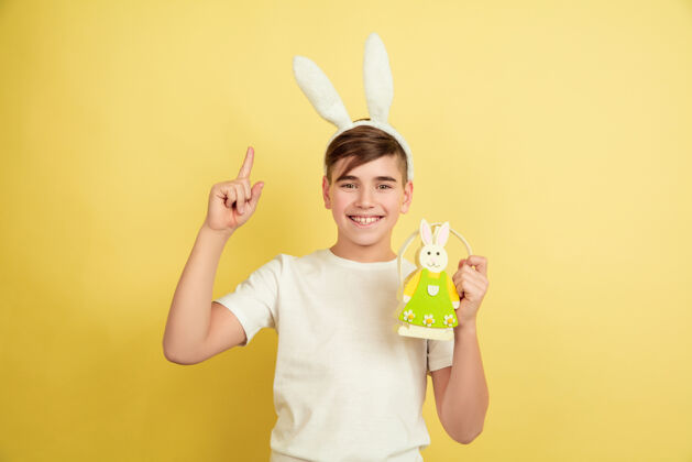 搞笑指向上装饰白人男孩作为一个复活节兔子在黄色的工作室背景复活节快乐的问候美丽的男模人类情感的概念 面部表情 节日复制空间面部狩猎强壮