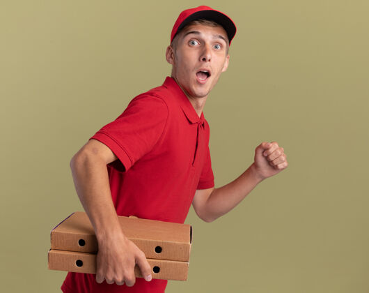 披萨惊讶的年轻金发送货男孩站在一边拿着披萨盒假装运行在橄榄绿假装送货站着