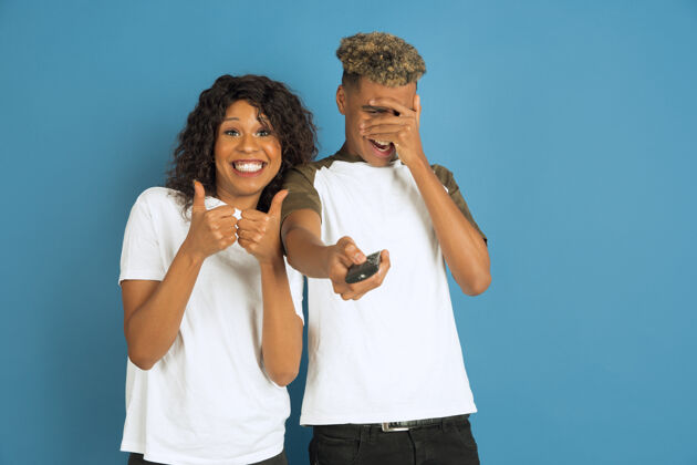 化妆年轻感性的非裔美国人男女在蓝色背景上摆姿势美丽的情侣人类情感的概念 面部表情 关系 广告一起看电视 她最喜欢的频道在一起笑情感