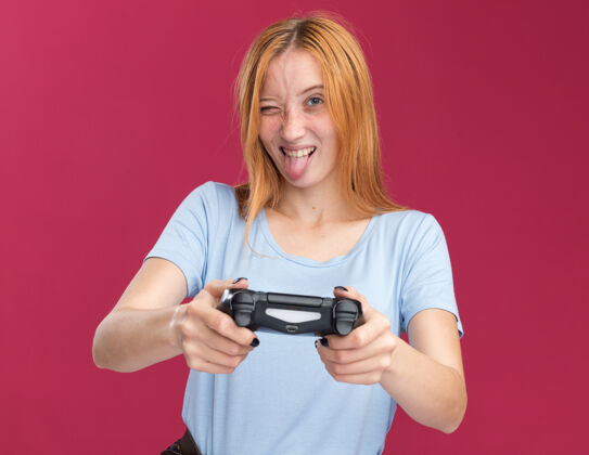 控制器快乐的年轻红发姜红色雀斑女孩结结巴巴的舌头 并举行了粉红色的游戏控制器游戏卡住年轻
