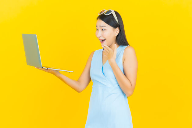 快乐一幅美丽的亚洲年轻女子微笑的画像 黄色的隔离墙上挂着一台笔记本电脑兴奋工作情绪