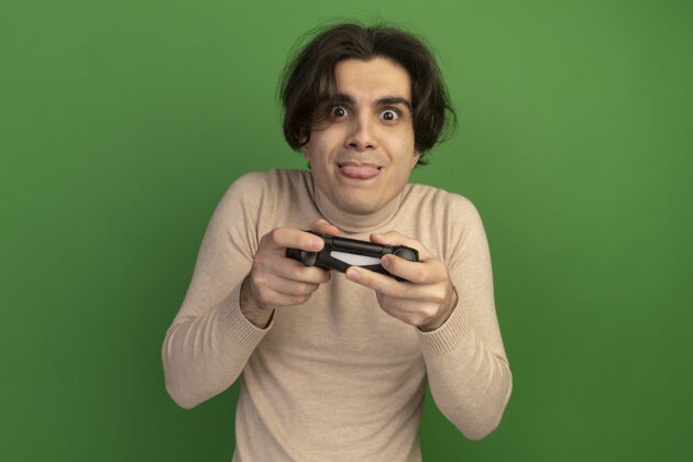 家伙兴奋的年轻帅哥拿着游戏控制器操纵杆隔离在绿色的墙上感觉表情姿势