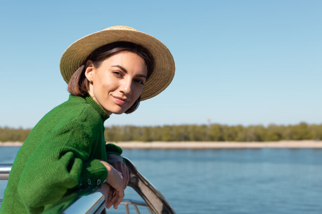 户外穿着绿色休闲毛衣 戴着帽子的时尚女士在户外的桥上欣赏河景 享受夏日阳光明媚的日子旅游城市女士