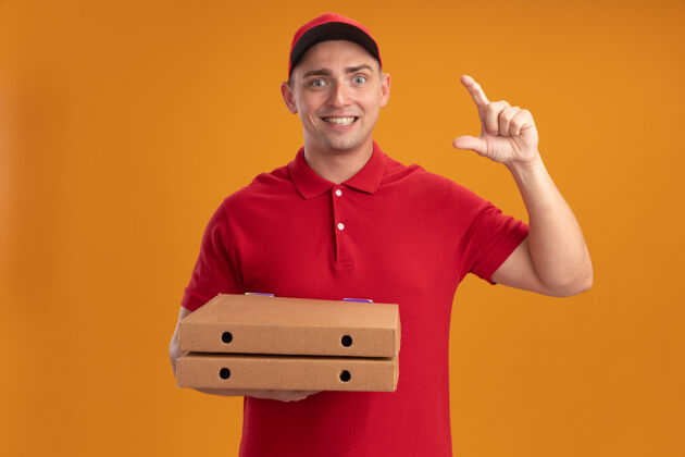 人微笑的年轻送货员身穿制服 头戴鸭舌帽 拿着披萨盒 在橙色的墙上显示大小男人脸拿着