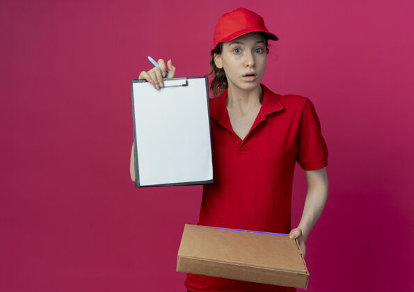 女孩令人印象深刻的年轻漂亮的送货女孩在红色制服和帽子举行比萨饼包装笔和显示剪贴板上的深红色背景与复制空间隔离剪贴板深红色显示
