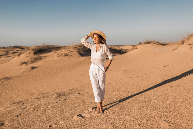 年轻一个穿着白色衣服 戴着草帽 在沙漠沙滩上行走的时尚美女旅行者迪拜热