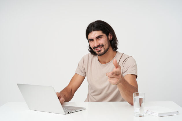 男性开朗的家伙 快乐的商人 黑头发和胡须办公室概念坐在工作场所在笔记本电脑上工作 隔着白墙服装人工作场所