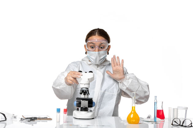 正面前视图女医生穿着特制的工作服 戴着口罩 用显微镜观察一种白色背景病毒-冠状病毒大流行穿着医生工作