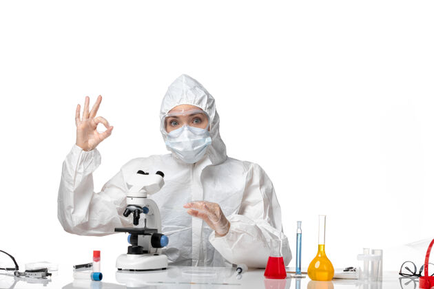 病毒正面图：女医生穿着防护服 戴着口罩 因为在白色办公桌上用显微镜观察病毒大流行 溅起病毒女医生药品视图