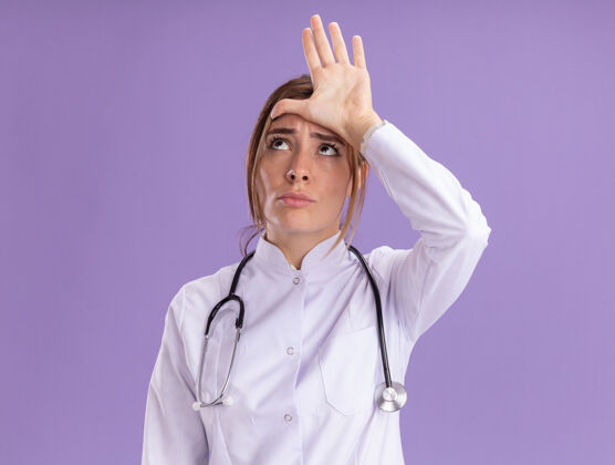 穿着想看看边上年轻的女医生穿着医用长袍 听诊器显示输的姿态孤立在紫色的墙上壁板脸医学