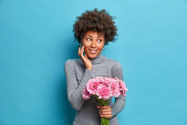 新鲜高兴的非洲裔美国妇女手持粉红色非洲菊花束非洲女孩高领毛衣