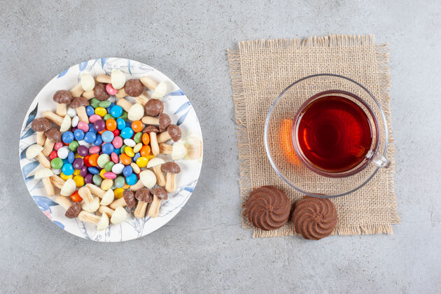 糖一盘糖果和巧克力蘑菇 旁边放一杯茶和两块饼干在大理石表面巧克力糕点饼干