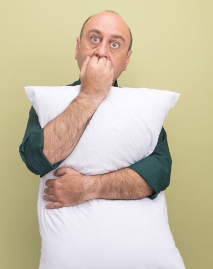 拥抱关切的中年男子穿着绿色t恤抱枕咬指甲隔离在橄榄绿的墙上中年关心枕头