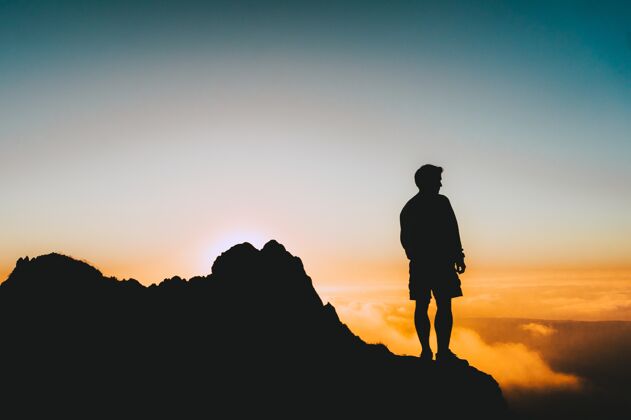 海岸一个人站在悬崖上看日落的剪影孤独岩石黄昏