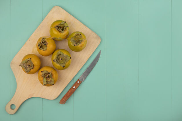 新鲜顶视图橙色生柿子水果在一个木制的厨房板上用刀在一个蓝色的木制桌子上复制空间木板景观顶部