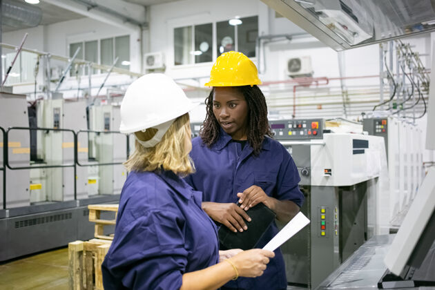 安全穿着安全帽和工作服的工厂女员工站在工厂地板上聊天工程站工厂