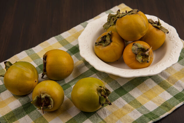 顶部新鲜柿子水果的顶视图在一个白色的碗里 柿子水果被隔离在木桌上的格子布上柿子水果橘子