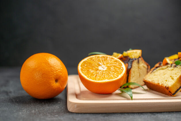 烘焙侧视图新鲜柠檬片和新鲜烤切碎蛋糕片在黑暗的桌子上可食用水果橙子切片