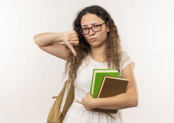 眼镜年轻漂亮的女学生戴着眼镜 背着书包 大拇指朝下 孤立地站在白色背景上拇指年轻背部