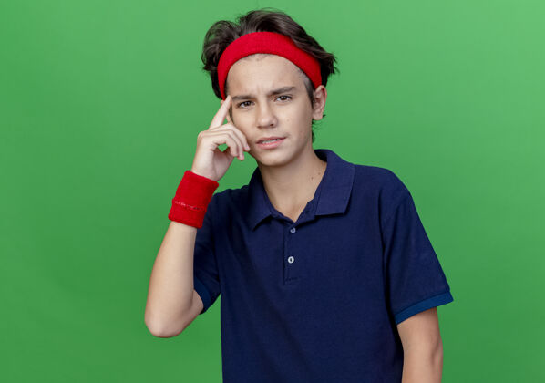 年轻自信的年轻帅气的运动男孩戴着头带和护腕 戴着牙套 看着前面做着独立思考的姿势 在绿色的墙上留着复制空间感觉男孩牙齿