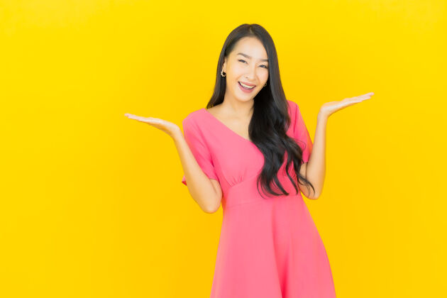 快乐黄色墙壁上 美丽的亚洲年轻女子身着粉色连衣裙微笑的画像微笑时尚黑发