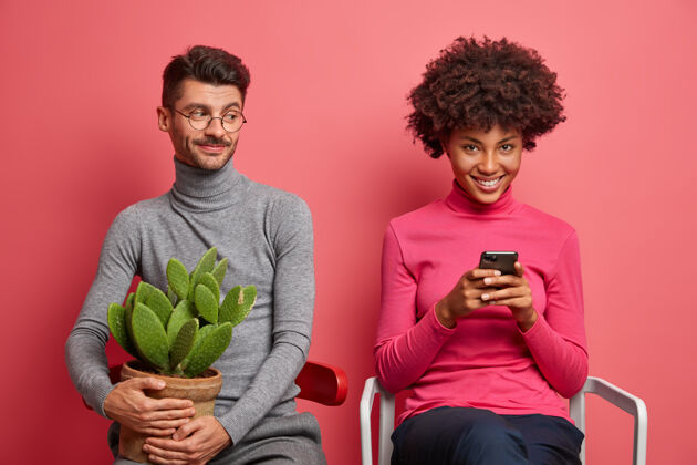 眼镜积极上瘾的年轻女子用手机上网她的男朋友坐在旁边拿着盆栽仙人掌 需要现场交流技术上瘾和关系概念家庭人房子