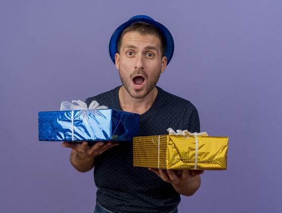 惊喜一个戴着蓝色帽子的白人帅哥拿着一个紫色背景的礼品盒 里面有一个复制空间持有男士礼物