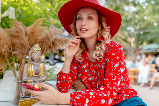 服装迷人的时尚金发微笑的女人在稻草红帽子和衬衫夏季时尚服装举行使用智能手机咖啡厅配件女孩女士