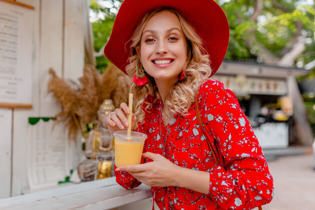 饮用迷人时尚的金发微笑女士 头戴草帽 身穿短衫 夏季时尚套装 饮用天然水果鸡尾酒冰沙时尚女士帽子