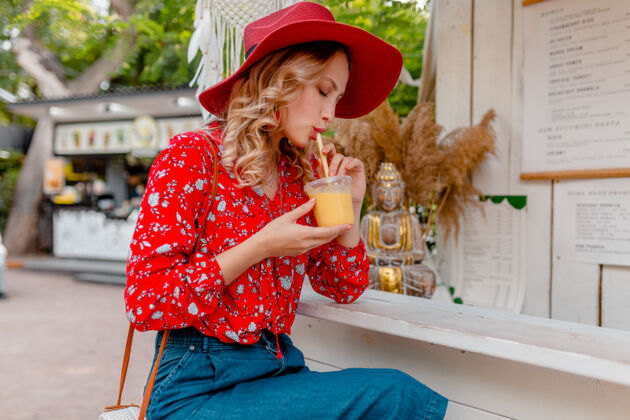明亮迷人时尚的金发微笑女士 头戴草帽 身穿短衫 夏季时尚套装 饮用天然水果鸡尾酒冰沙时尚饮用帽子
