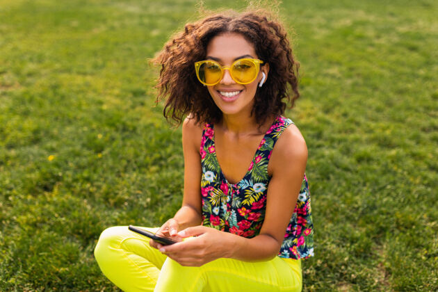 休闲年轻时尚微笑的黑人女子使用智能手机 通过无线耳机听音乐 在公园里玩得很开心女士非裔美国人耳机