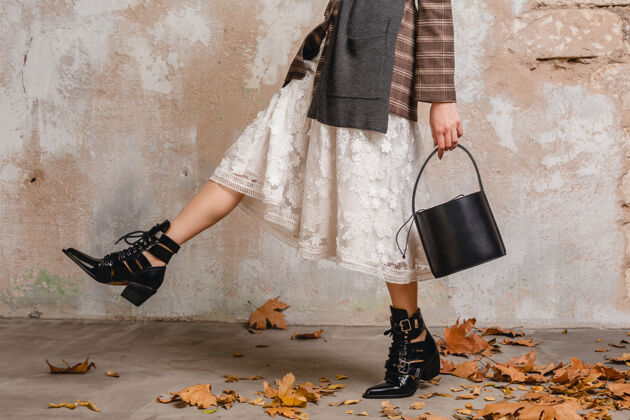 秋天一个穿着夹克的时髦女人穿着靴子 在街上靠着墙走来走去年轻包外套