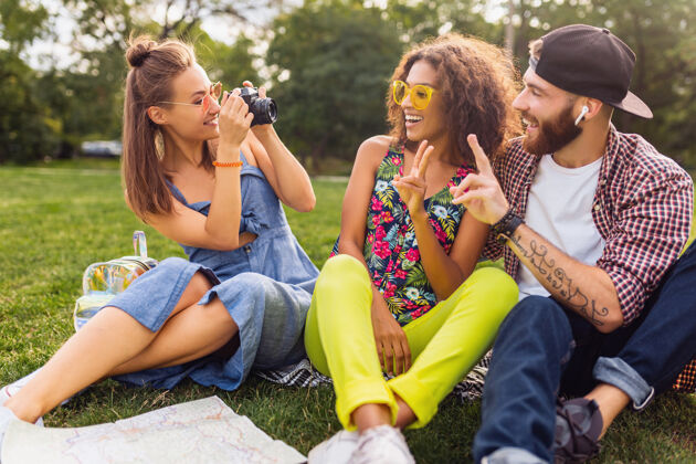 女人快乐的年轻朋友陪伴坐在公园里 男女同乐 缤纷的夏日潮人时尚风格 旅游拍照 谈笑风生友谊兴奋旅行