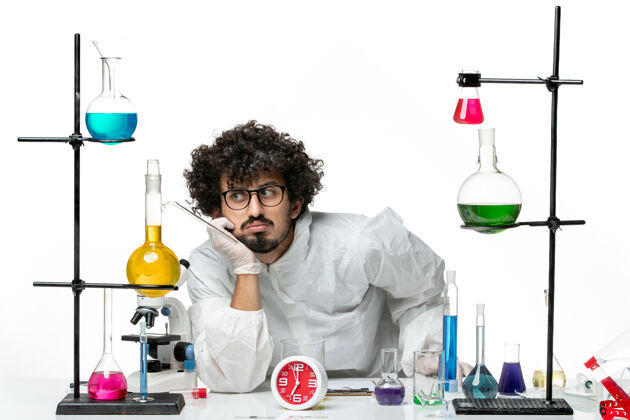 烧杯正面图身穿白色特殊套装的年轻男性科学家围坐在桌子旁 拿着白色墙壁上的解决方案科学covid化学实验室玻璃实验室容器