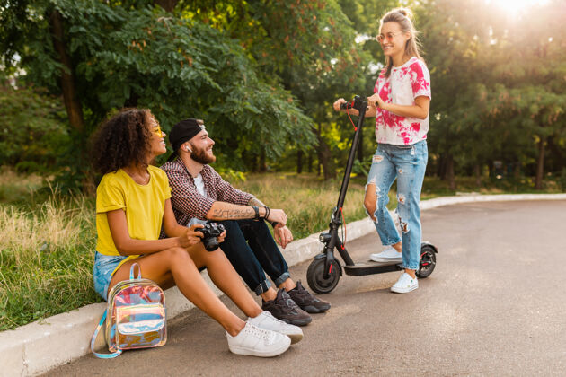 街道快乐的年轻朋友们坐在公园的草地上 带着电动脚踏车微笑着 男女同乐车辆欢呼黑色