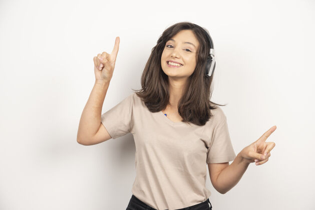 肖像穿着米色衬衫的可爱女人在白色背景下用无线耳机听音乐时玩得很开心年轻旋律女性
