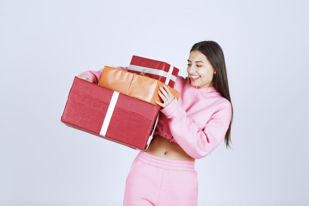 员工穿着粉色睡衣的女孩手里拿着多个红色礼盒 心情很开心年轻女人服装