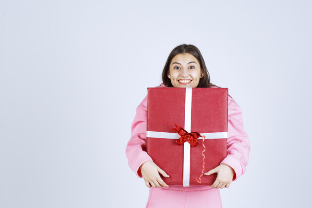 人穿着粉色睡衣的女孩抱着一个大大的红色礼盒 微笑着照片庆祝成人