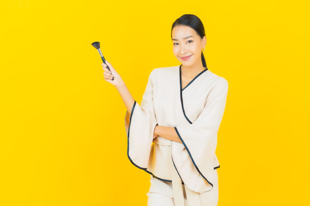脸美丽的亚洲商界年轻女性的画像 黄色墙上有化妆刷社交时尚评论