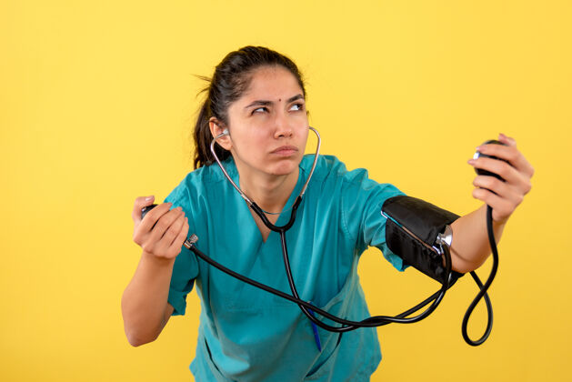 医生正面图体贴的年轻女医生 血压计在黄色背景上人制服思想
